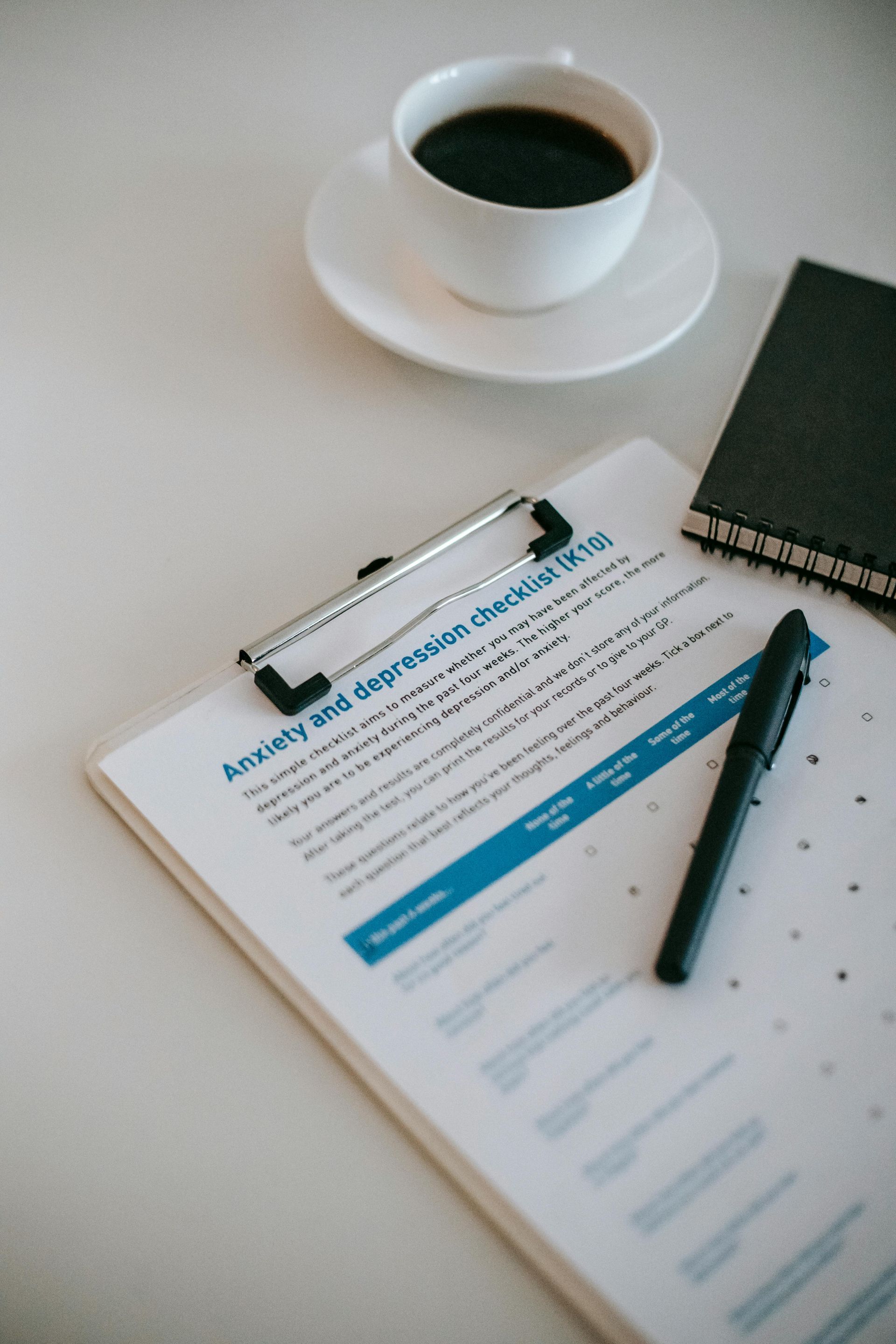 A clipboard with a pen and a cup of coffee on a saucer as part of assessment process for counseling intensive.
