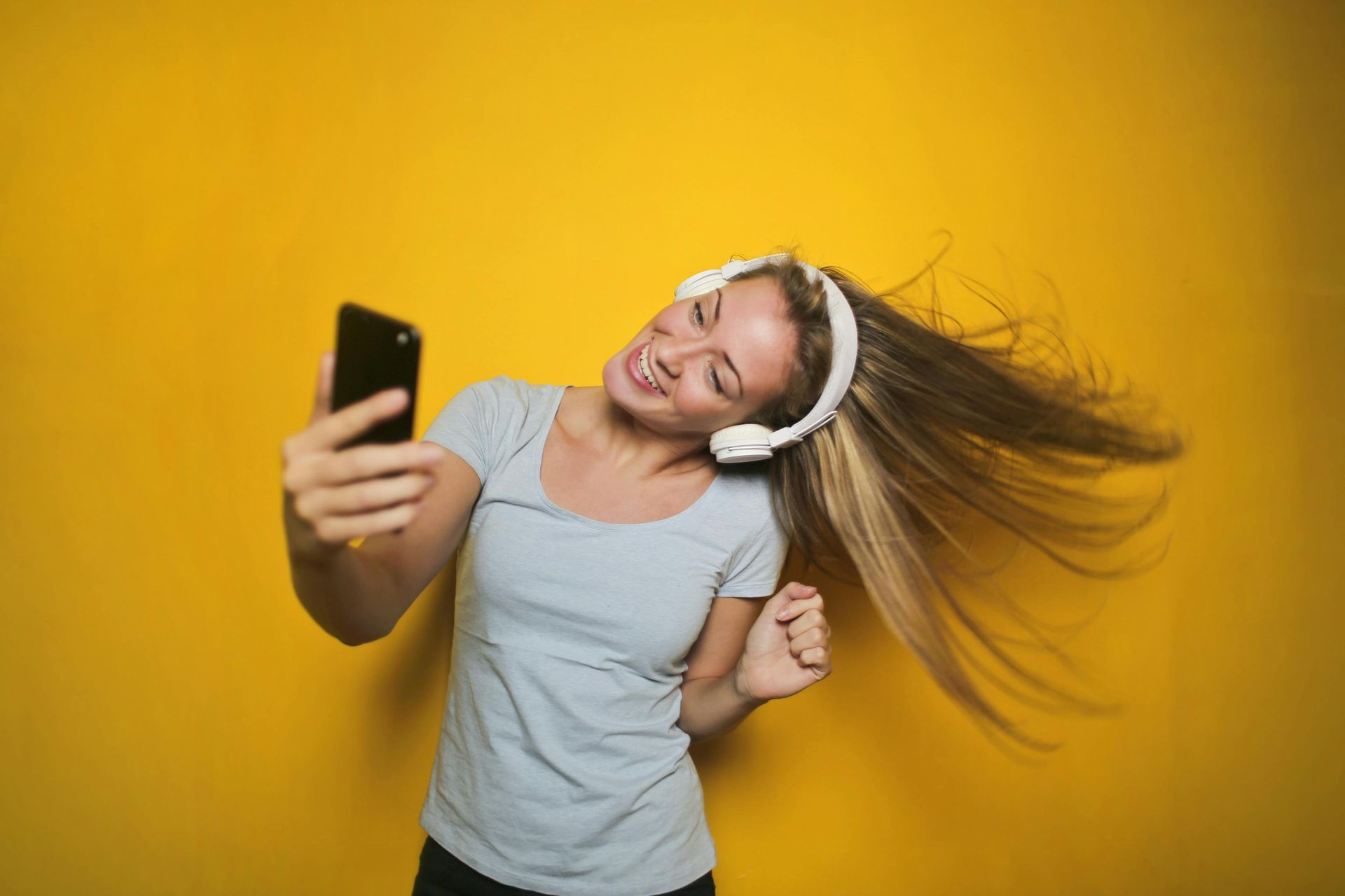 A woman wearing headphones is taking a selfie with her phone.