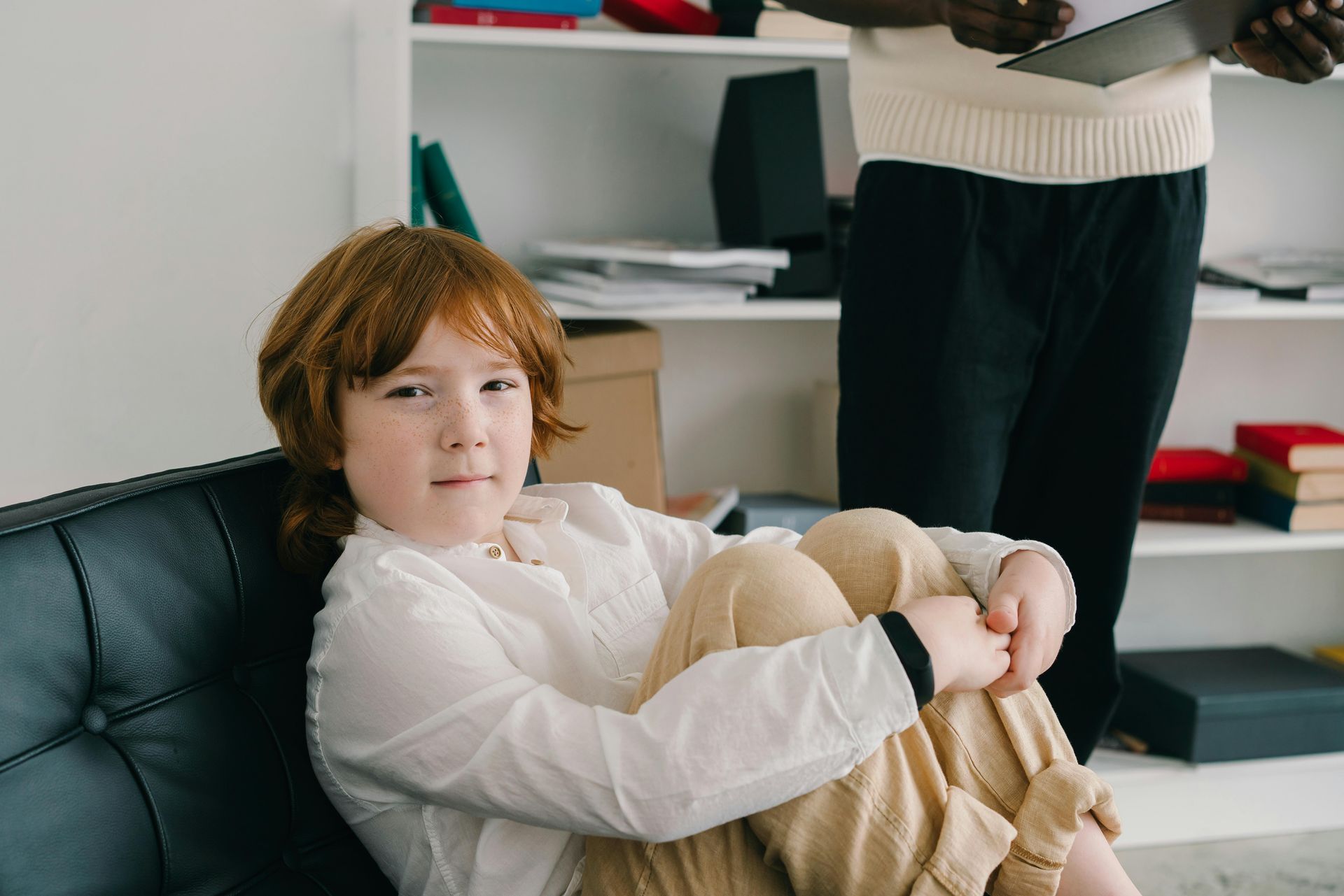 A young boy is sitting on a couch with his legs crossed at counseling for children in DFW.