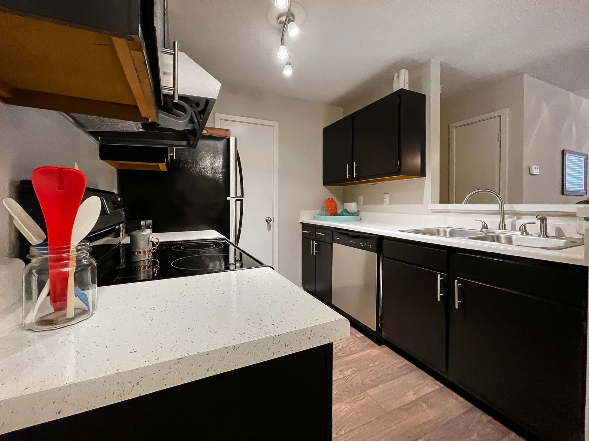 Modern apartment kitchen with black cabinets, white speckled countertops, and a stainless steel sink.