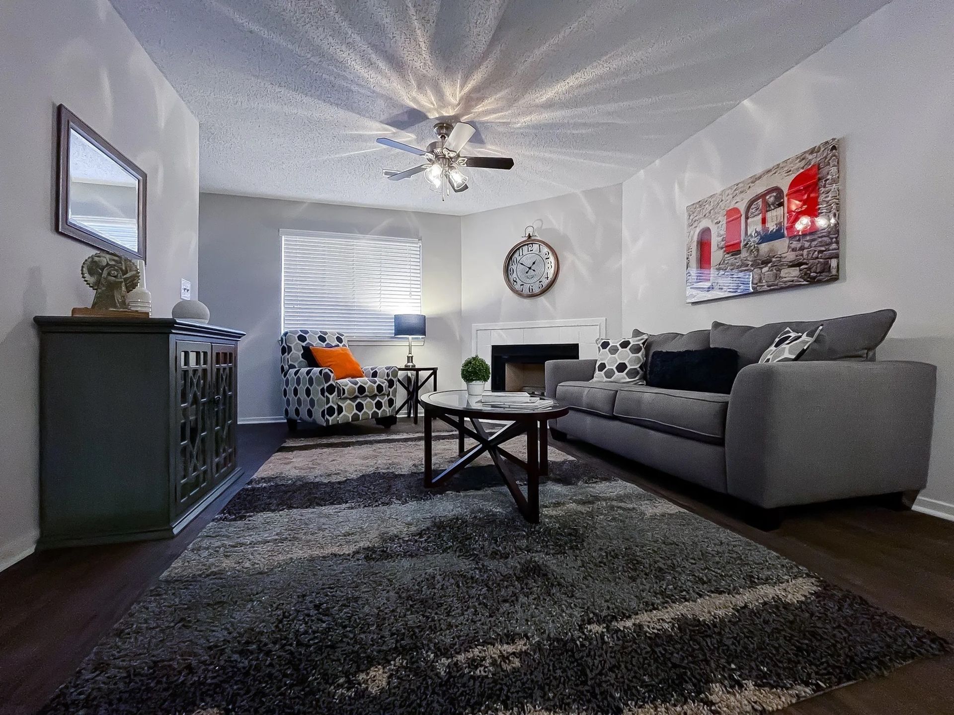 Cozy living room with a gray sofa, patterned armchair, coffee table, fireplace, and wall art.