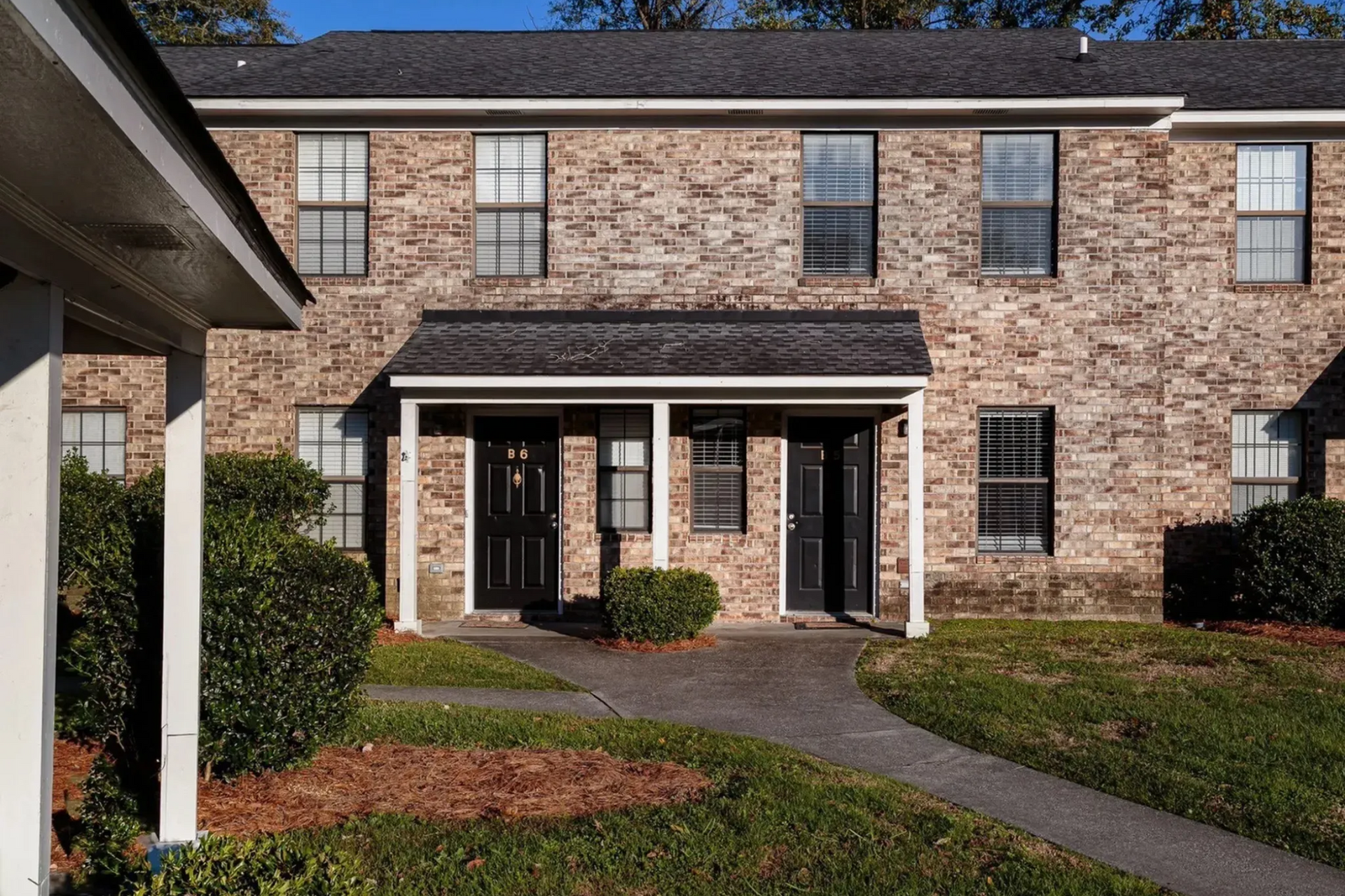 Exterior view of a two-story brick apartment building with a pathway and landscaping at Plantation Flats in North Charleston, SC.