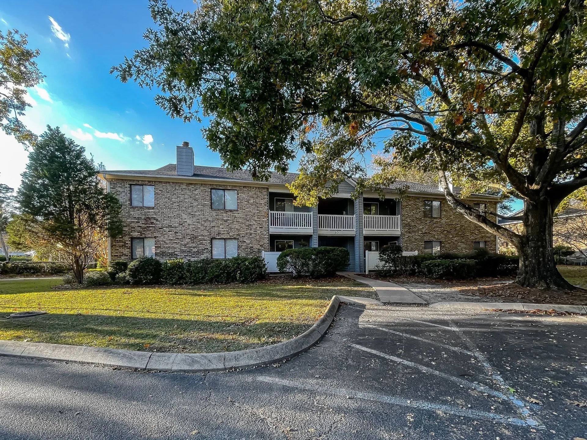 Exterior view of a two-story brick apartment building with balconies and surrounding trees.