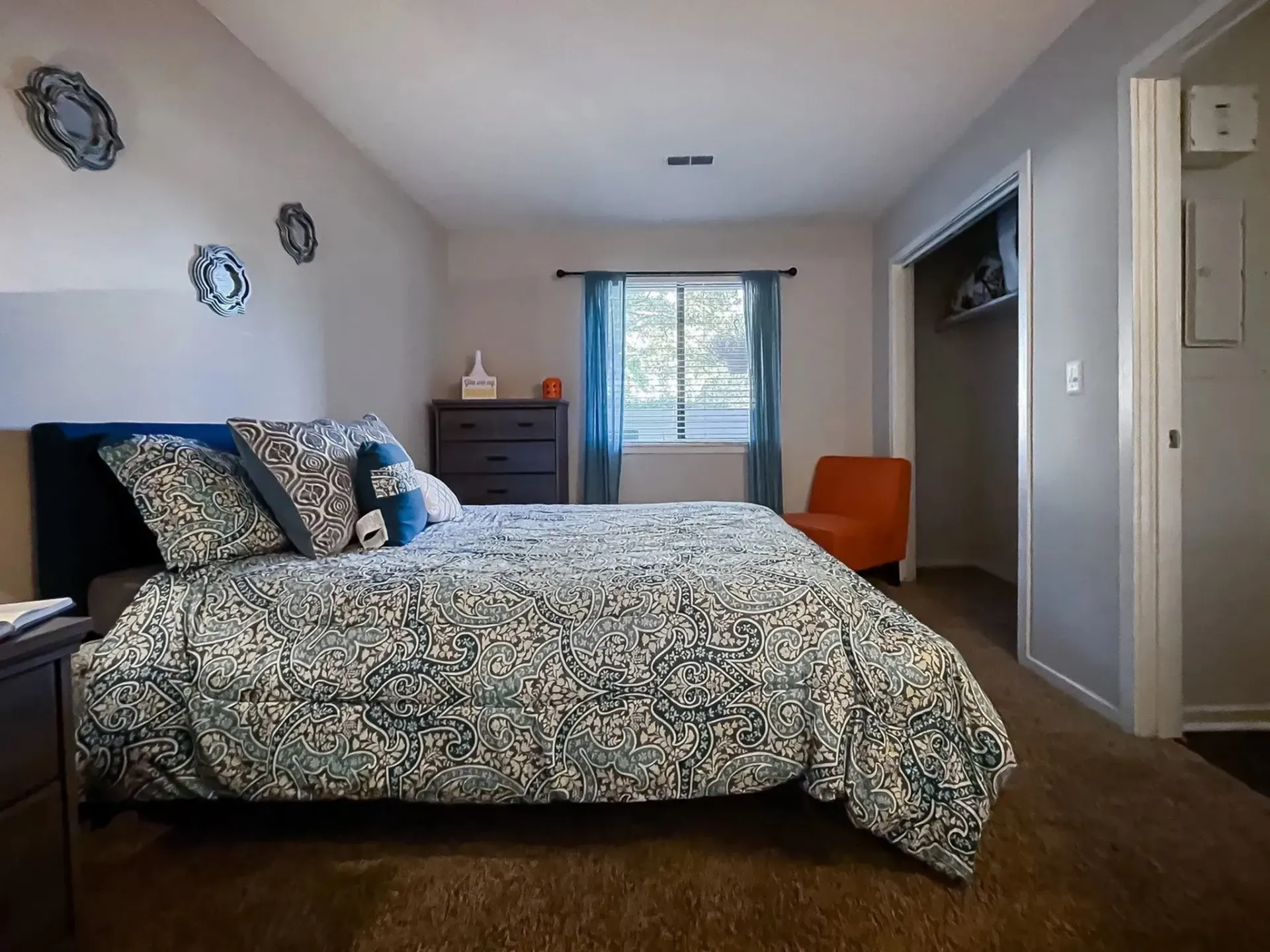 Bedroom with bed, dresser, window, chair, and closet. Blue, white, orange, and brown hues.