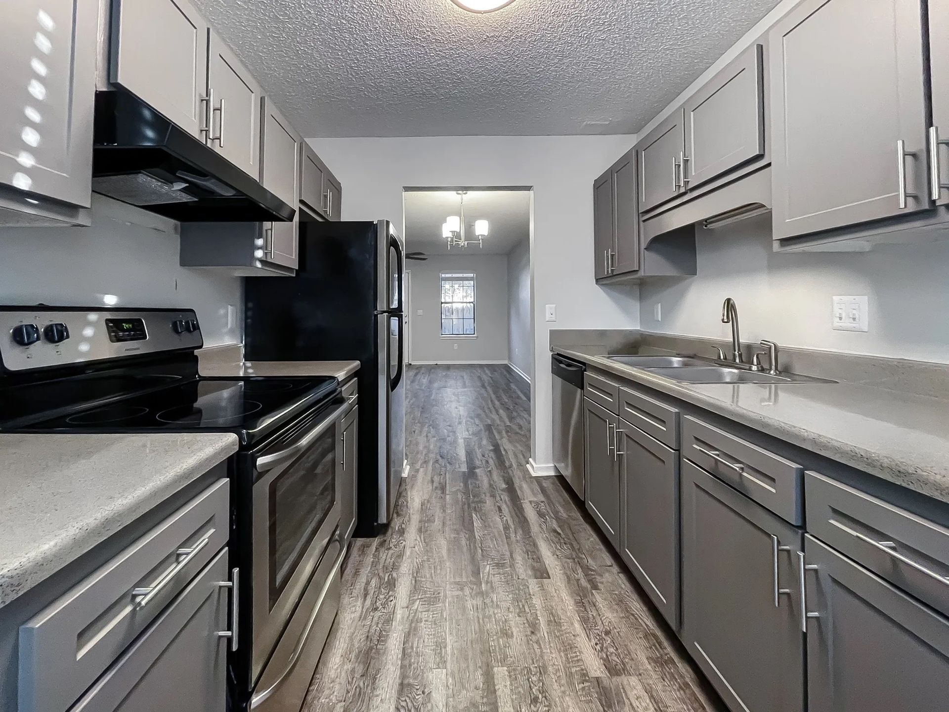 Galley-style kitchen in an apartment with grey cabinets, stainless steel appliances, and a double sink.