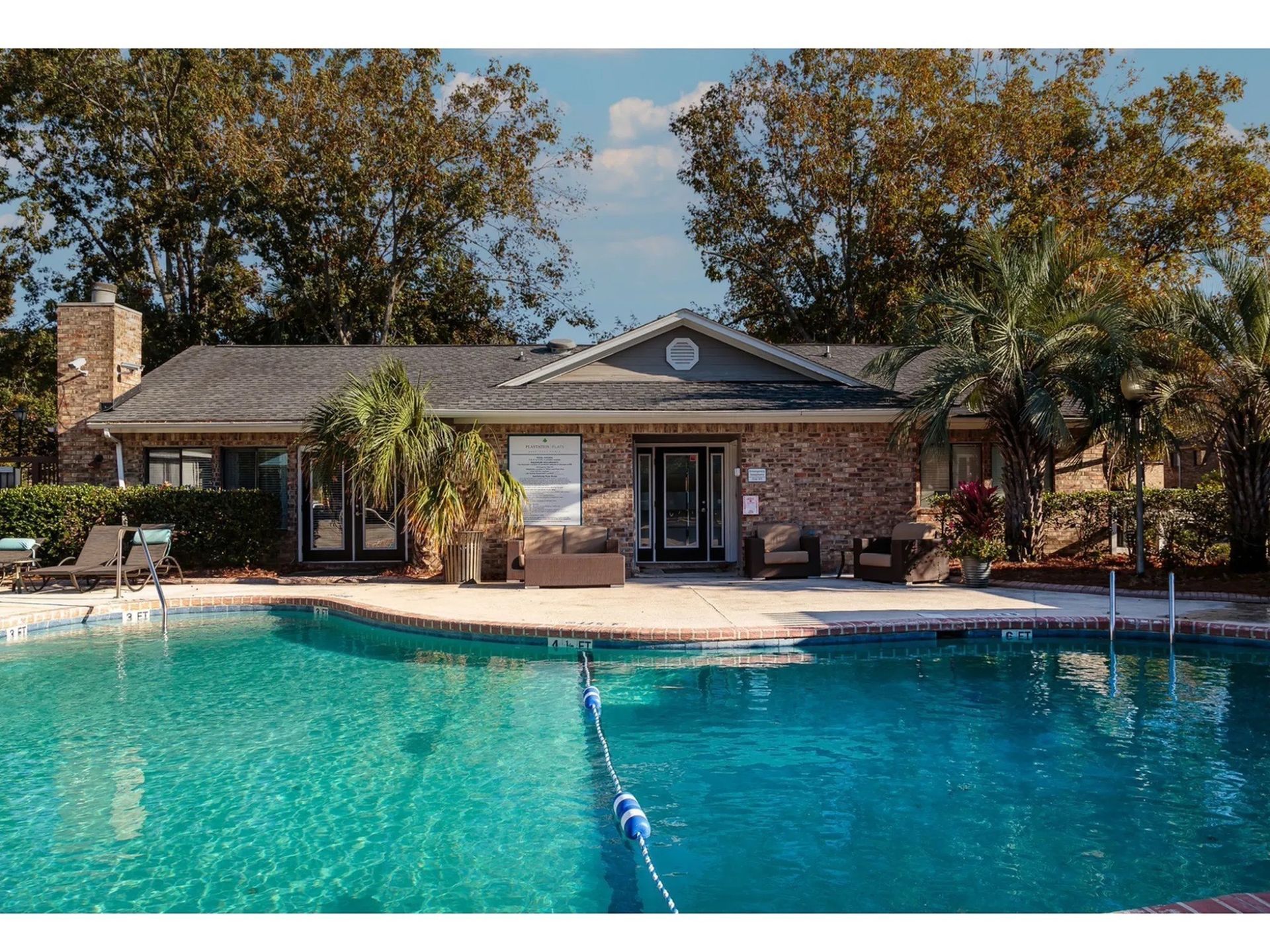 Outdoor apartment community pool with lounge seating, palm trees, and clear blue water.