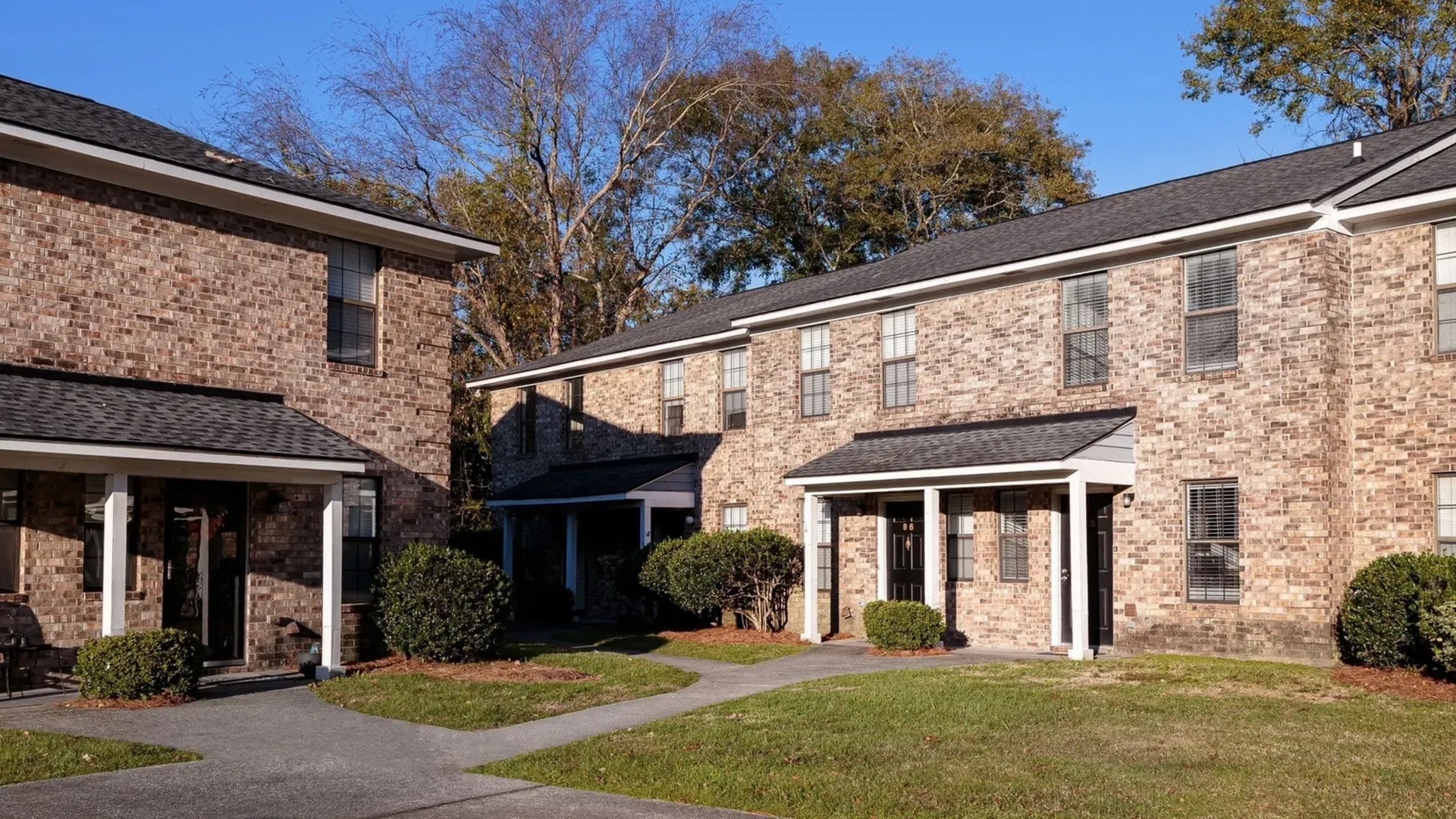 Exterior view of brick apartment buildings with pathways and greenery at Plantation Flats in North Charleston, SC.