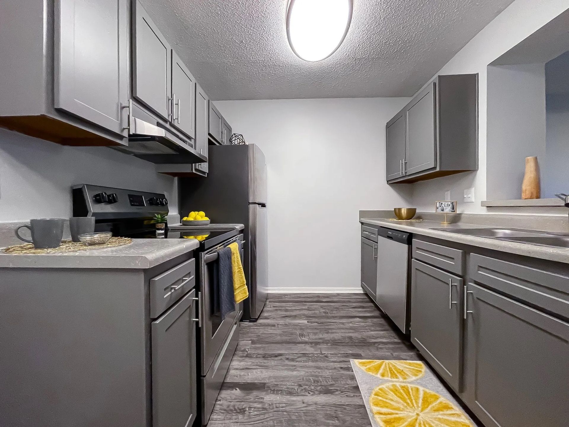 Galley-style kitchen in a modern apartment with gray cabinets, stainless appliances, and a yellow towel.