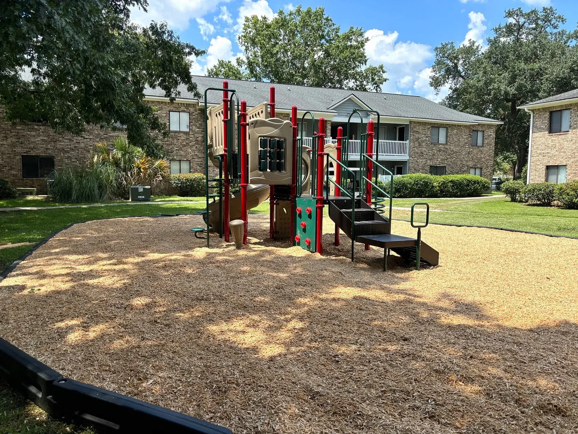Outdoor playground in an apartment community courtyard with mulch and surrounding brick buildings.