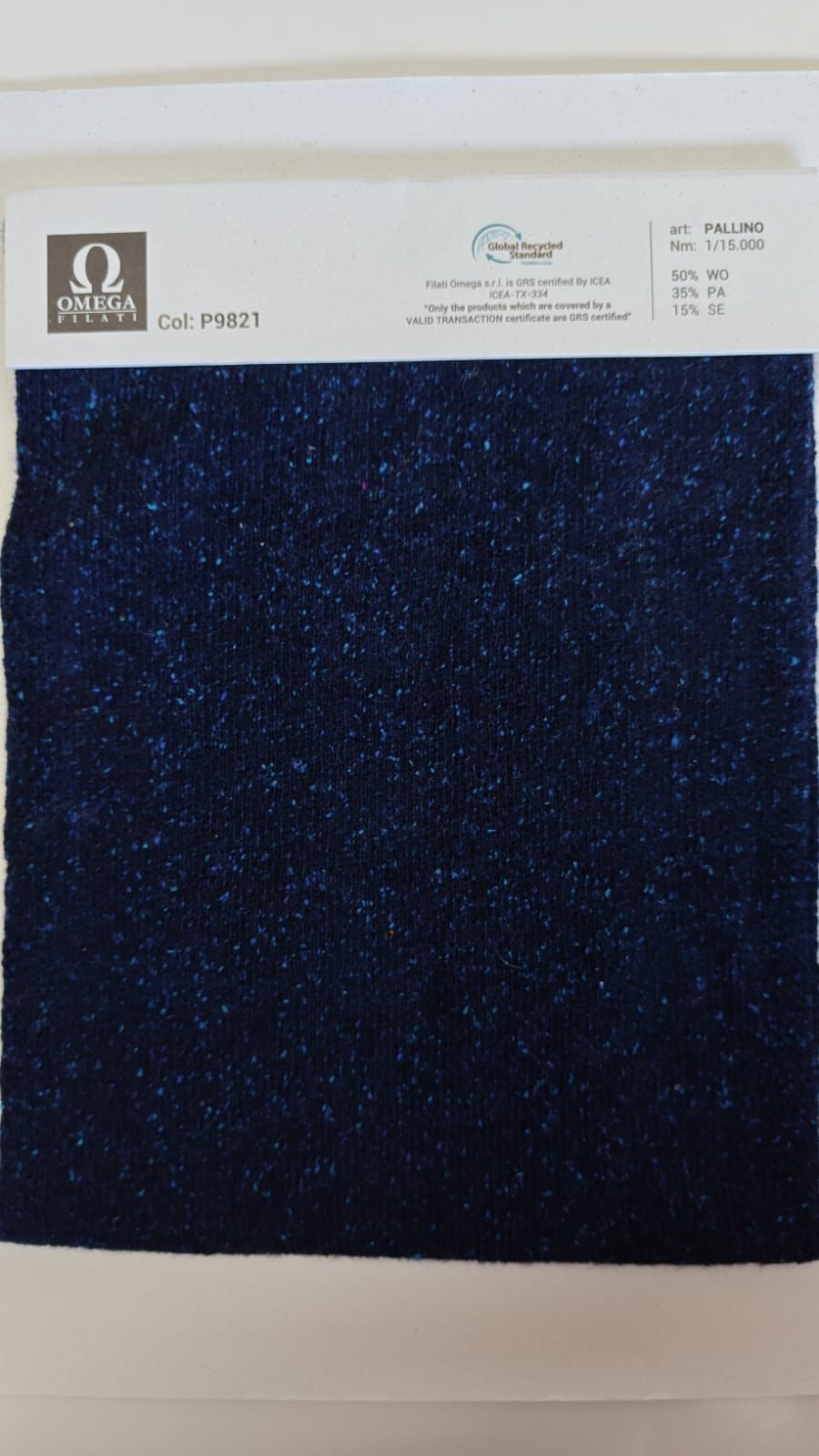 Muestra de tela azul oscuro con etiqueta blanca, salpicada de pequeñas motas.