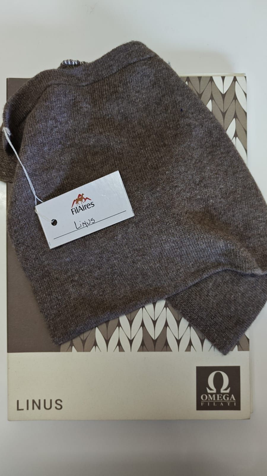 Gorro de punto marrón con etiqueta en una caja que dice 