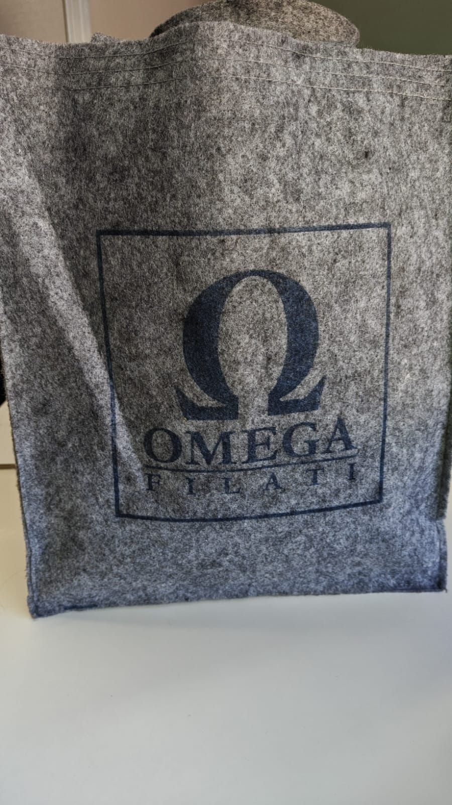Bolso tote de fieltro gris con el logotipo de Omega y la palabra 