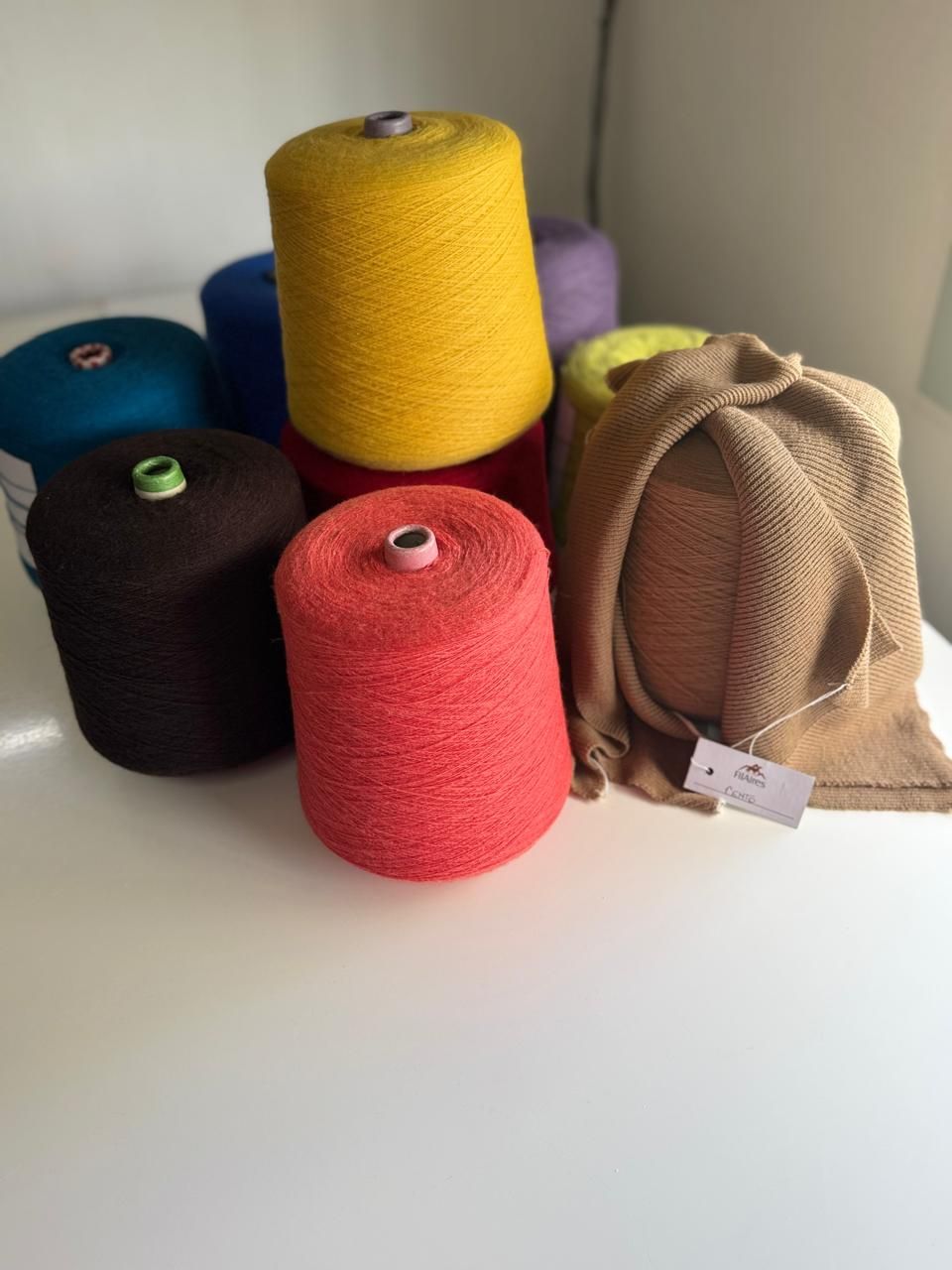 Carretes de hilo de colores dispuestos sobre una superficie blanca, con una bufanda doblada a la derecha.
