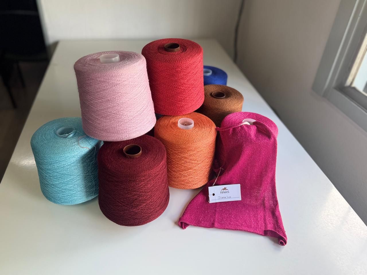 Carretes de hilo de colores: rosa, rojo, naranja, marrón, azul y verde azulado, sobre una superficie blanca.