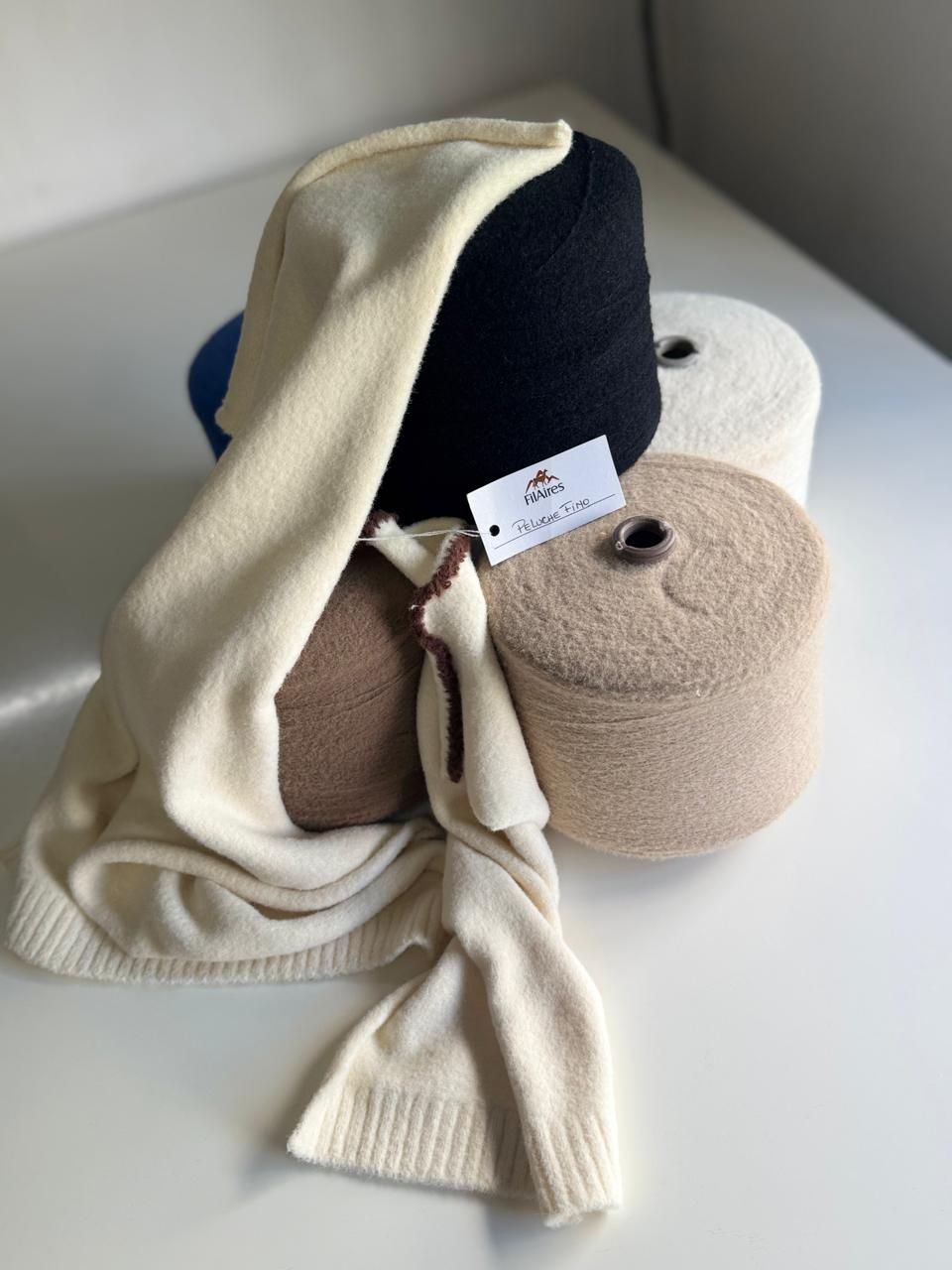 Bobinas de hilo en varios colores neutros, una bufanda de punto de color claro está drapeada sobre algunas de las bobinas.