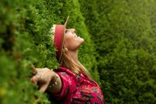 Une femme se tient à côté d'un buisson, les bras tendus.