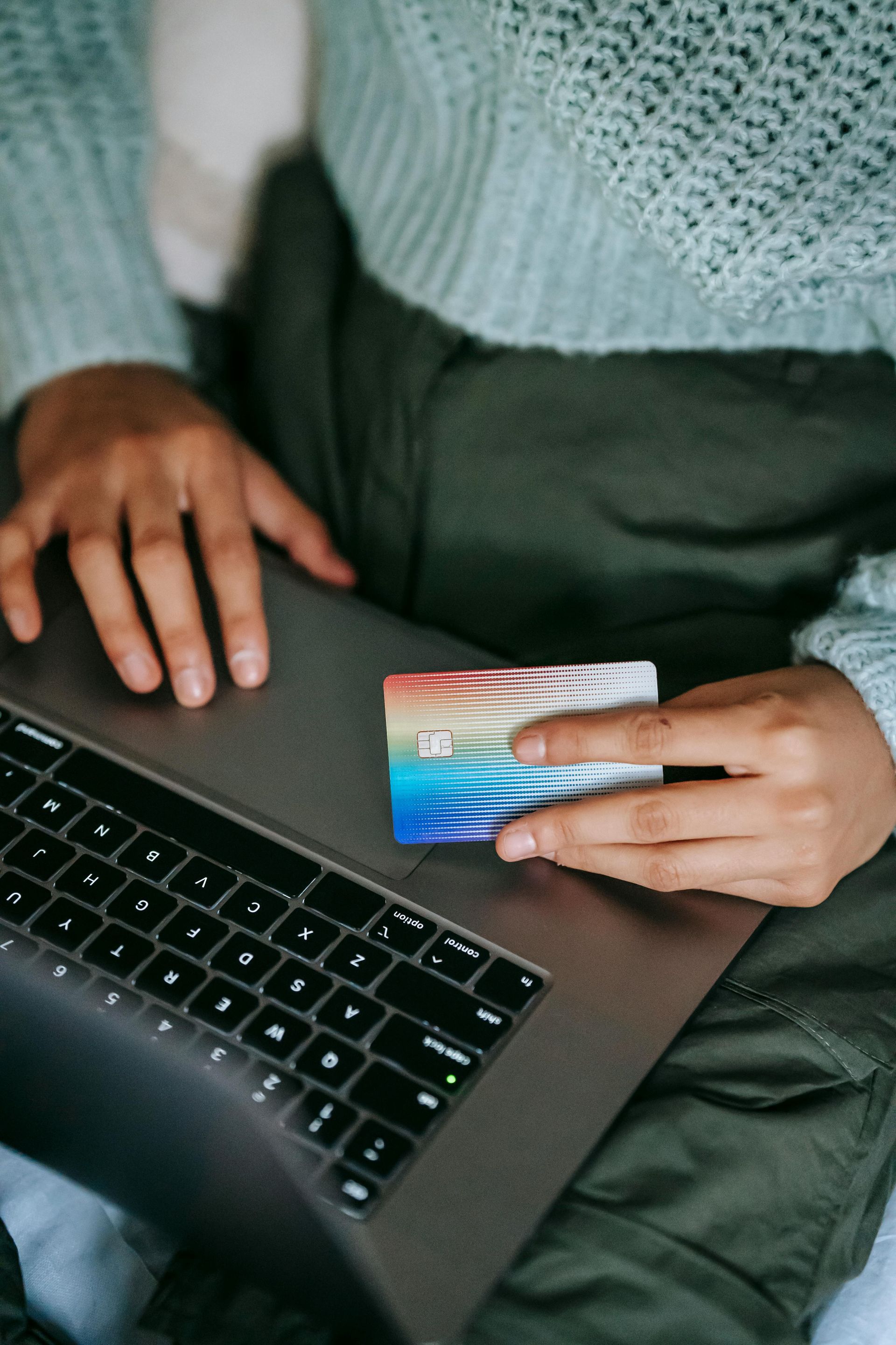 Une personne tient une carte de crédit devant un ordinateur portable.