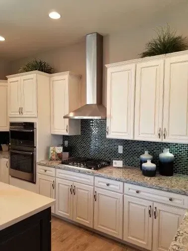 A kitchen with white cabinets , granite counter tops , a stove , and a hood.