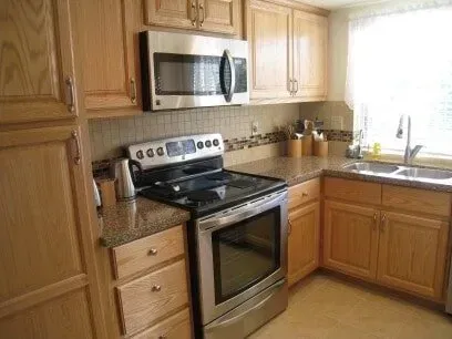 A kitchen with a stove , microwave , sink and wooden cabinets.