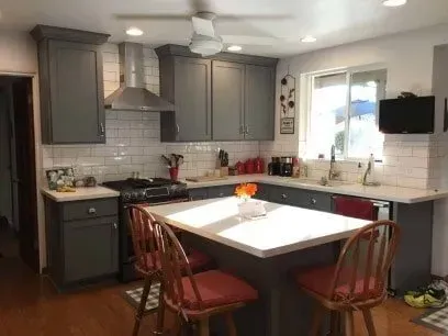 A kitchen with gray cabinets , a stove , a sink , and a large island.