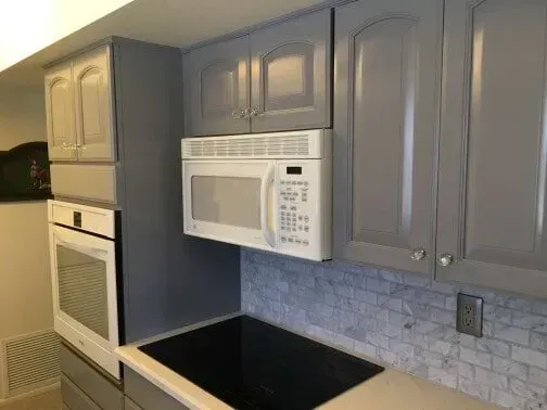 A kitchen with gray cabinets , a microwave oven , and a stove top oven.