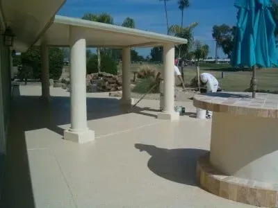 A man is painting a patio with a blue umbrella in the background.