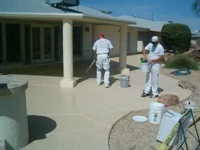 Two men are painting a patio in front of a house.