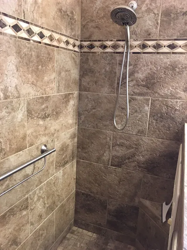 A walk in shower with a hand rail and a shower head.