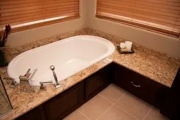 A bathtub is sitting on top of a granite counter in a bathroom next to a window.