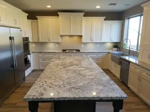 A kitchen with white cabinets , granite counter tops , stainless steel appliances and a large island.