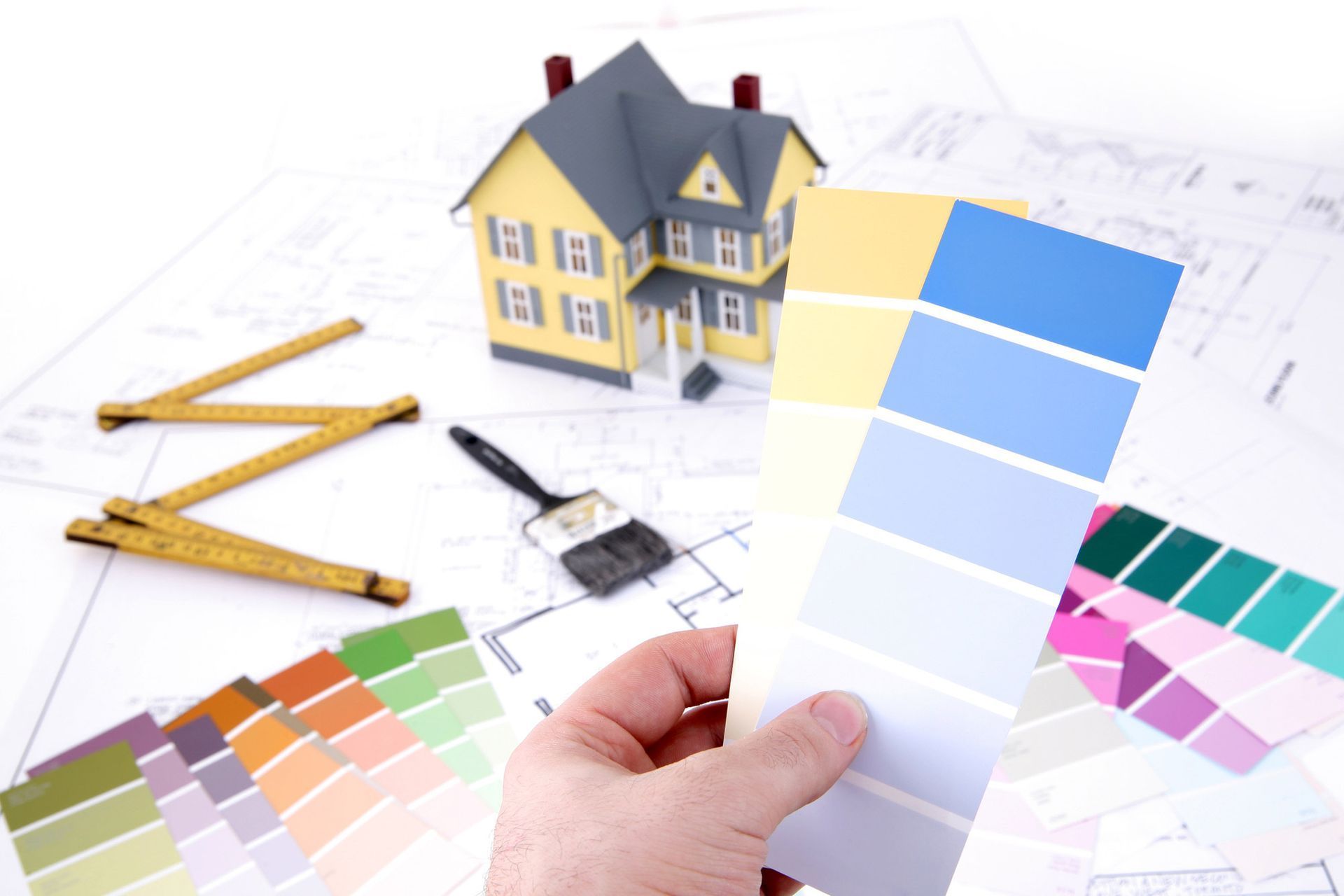 A person is holding a swatch of paint in front of a model house