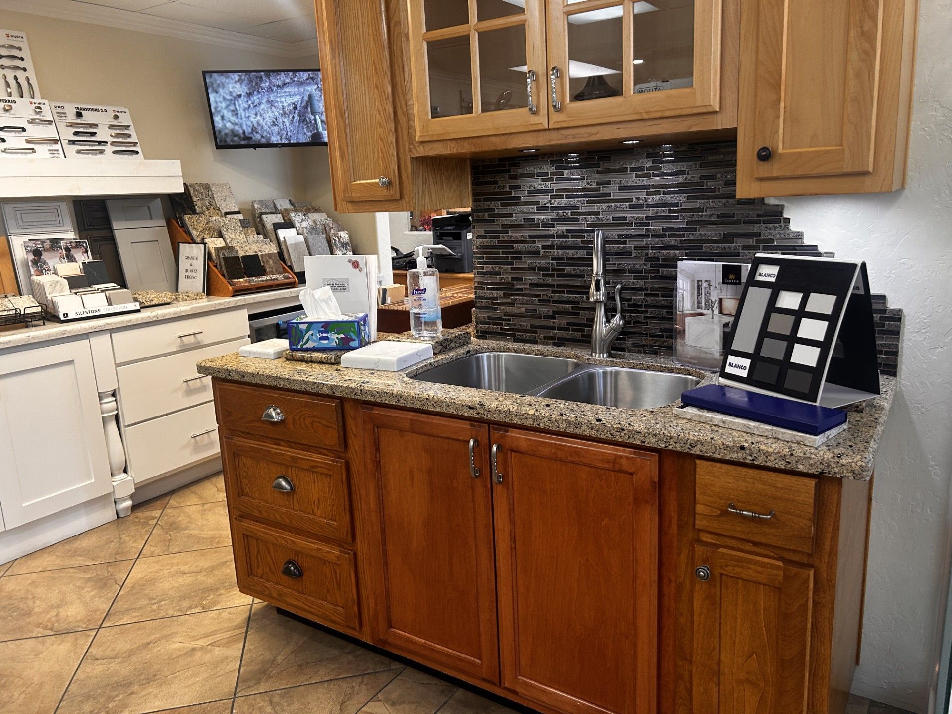 Kitchen display with sink, cabinets, tile samples, and a small TV.