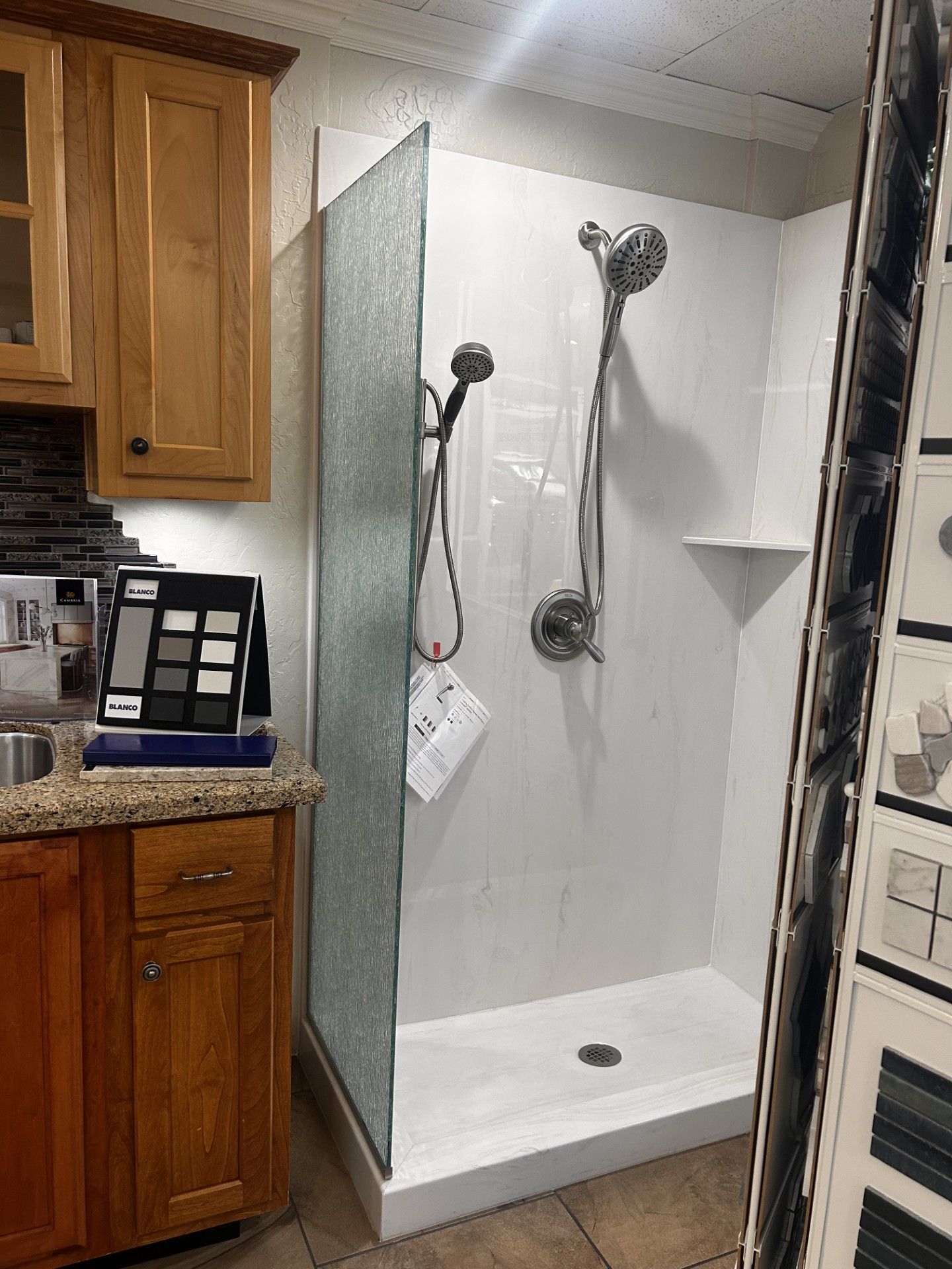 Shower stall with white walls, glass door, and showerheads. Wood cabinetry is to the left.