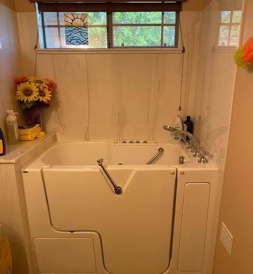 White walk-in tub in a bathroom with a window, flowers, and soap dispenser.