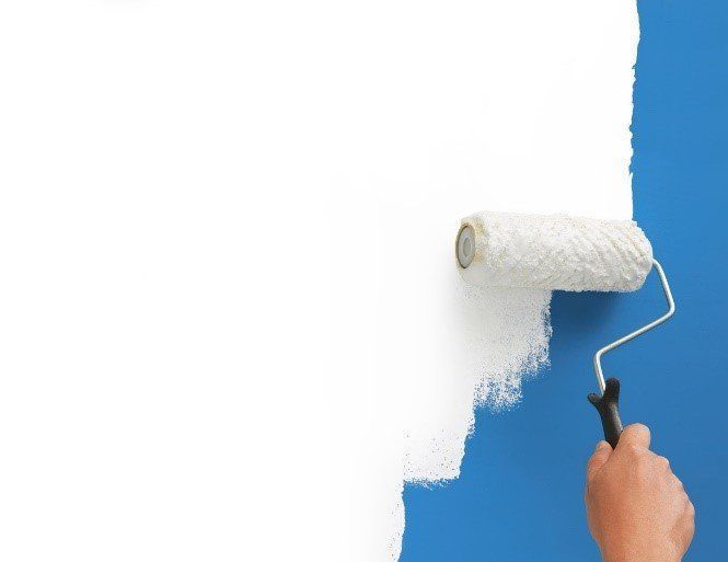 A person is painting a blue wall with white paint