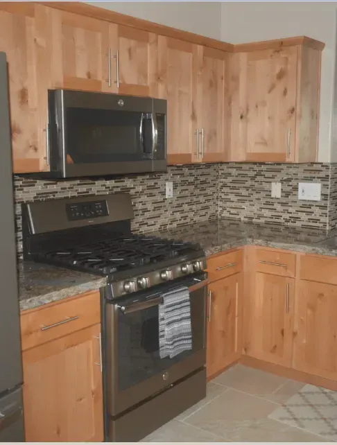 A kitchen with wooden cabinets and a stove, and a microwave.
