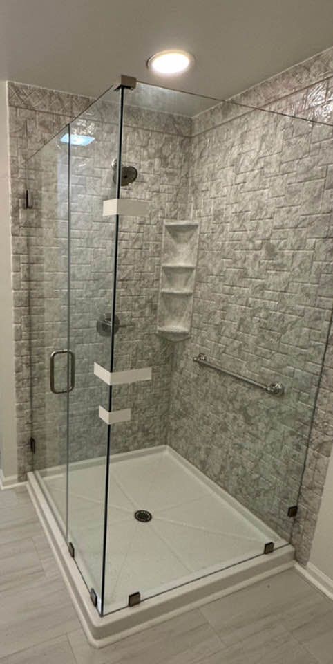 A modern, glass-enclosed shower with gray tiled walls, a white base, and built-in shelves.