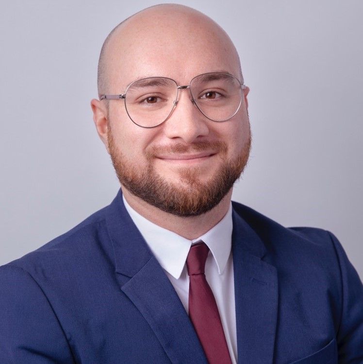 A bald man with glasses and a beard is wearing a suit and tie.