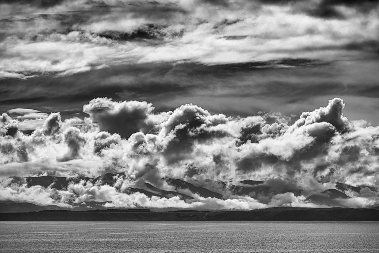 A black and white photo of a cloudy sky over a body of water.