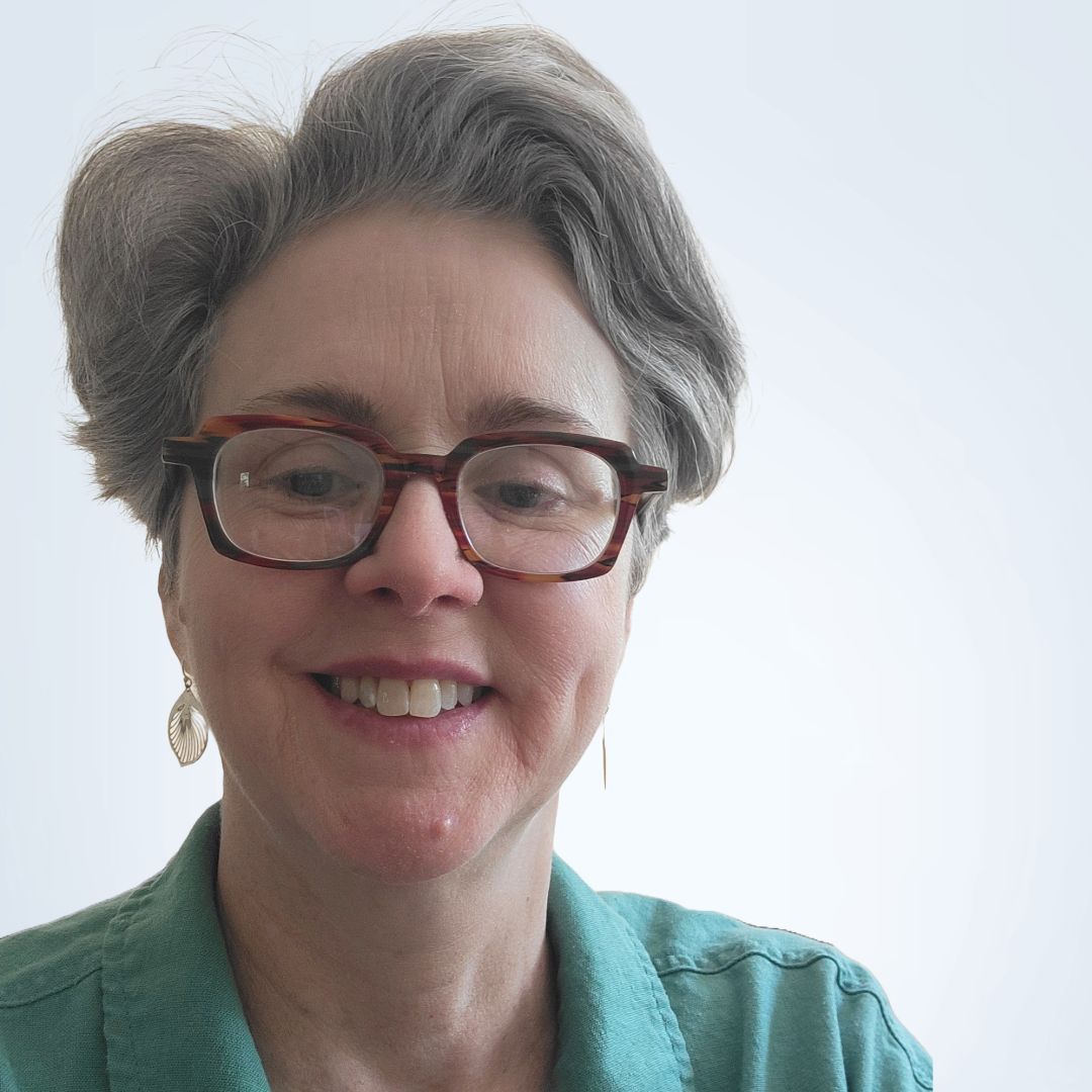 Woman with shoulder-length blonde hair smiling; wearing a gray sweater with buttons.
