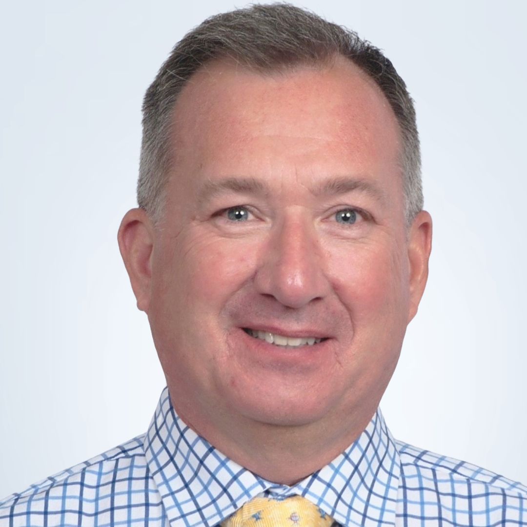 Man in blue patterned shirt smiling, looking at the camera.