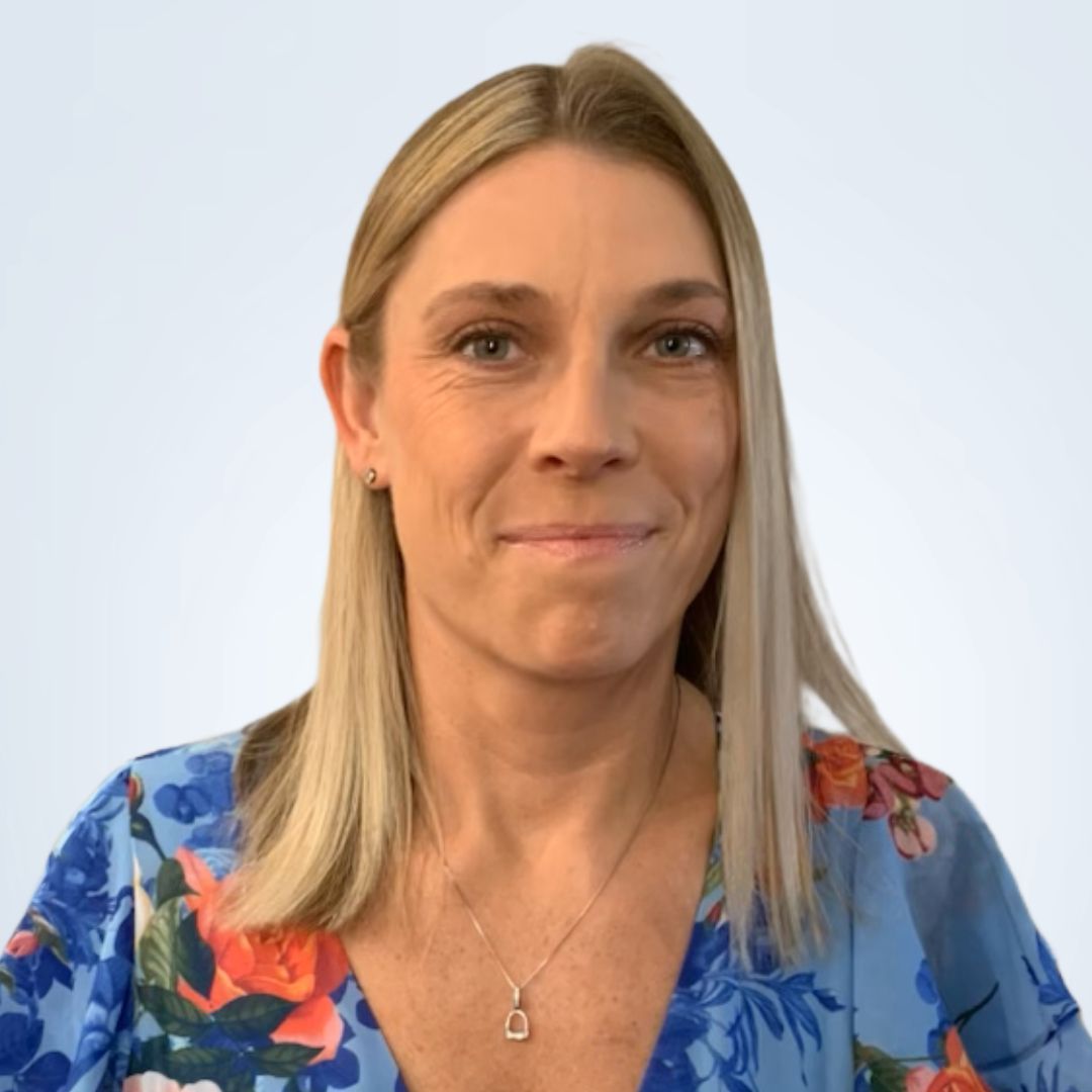Woman with wavy blonde hair smiling, wearing a gray sweater with two buttons.