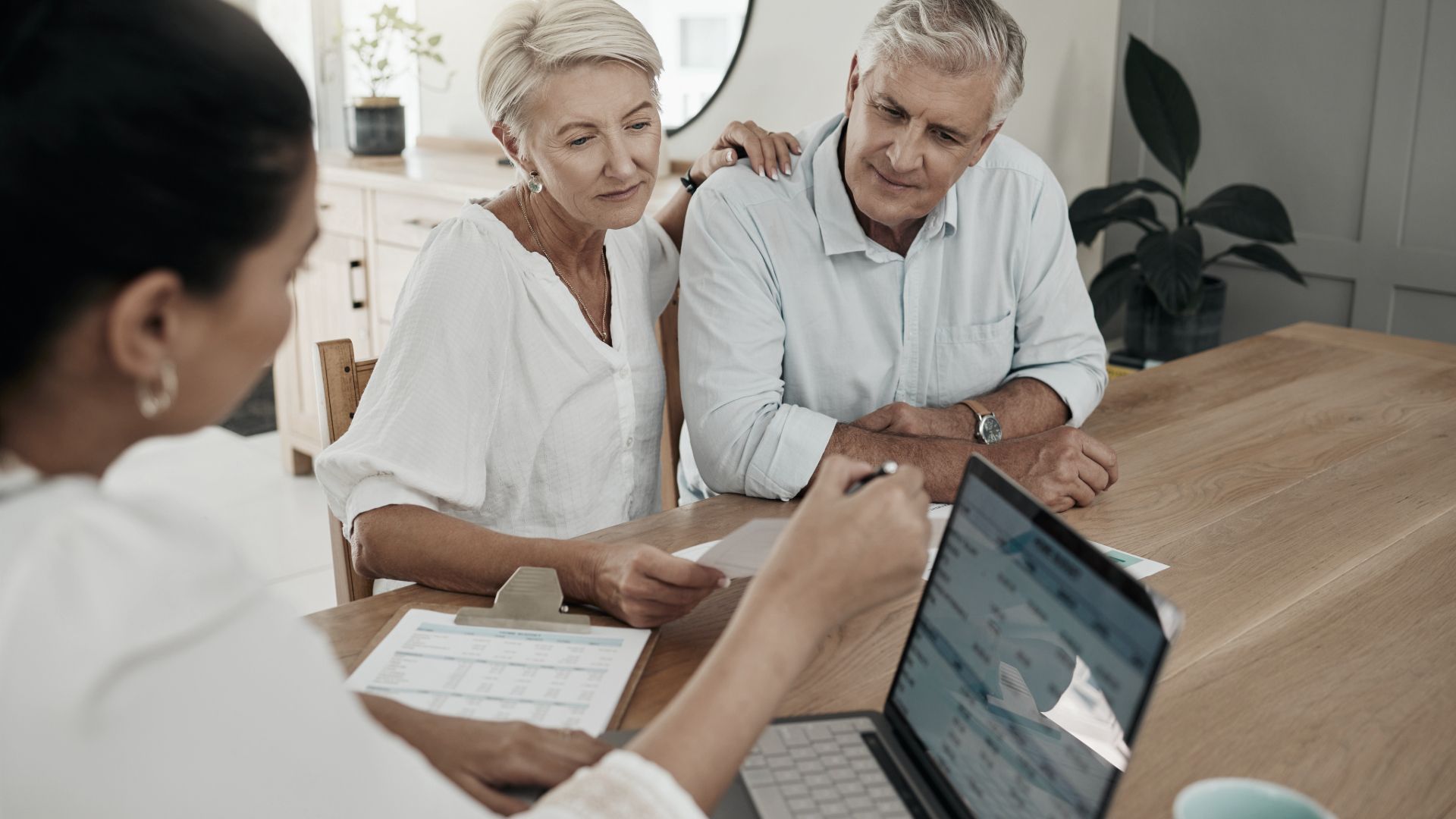 Woman showing papers on a laptop to a senior couple at a table.
