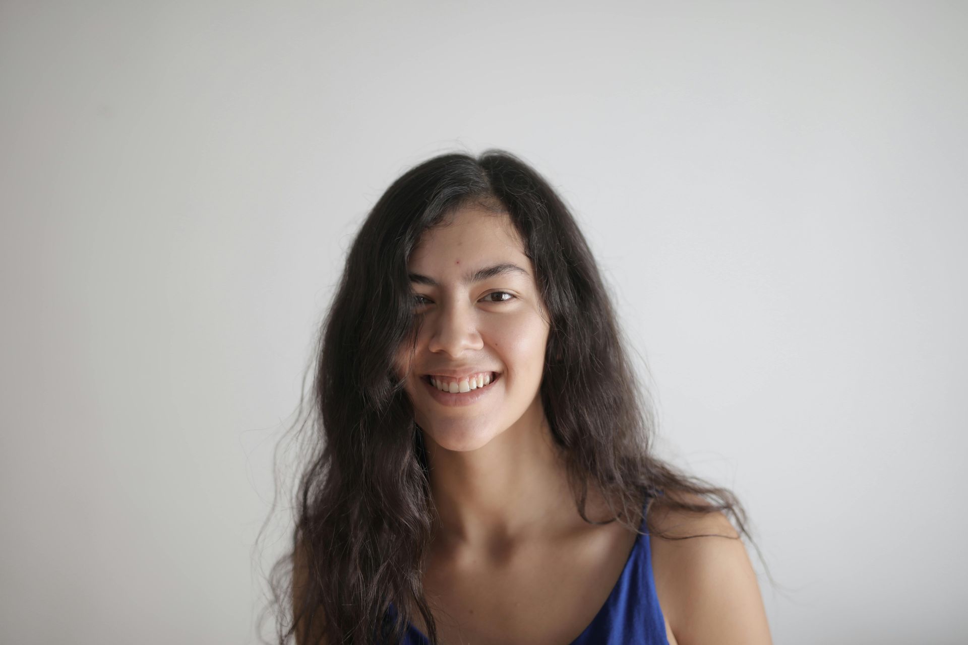 Woman with long dark hair, smiling, wearing a blue top against a white background.