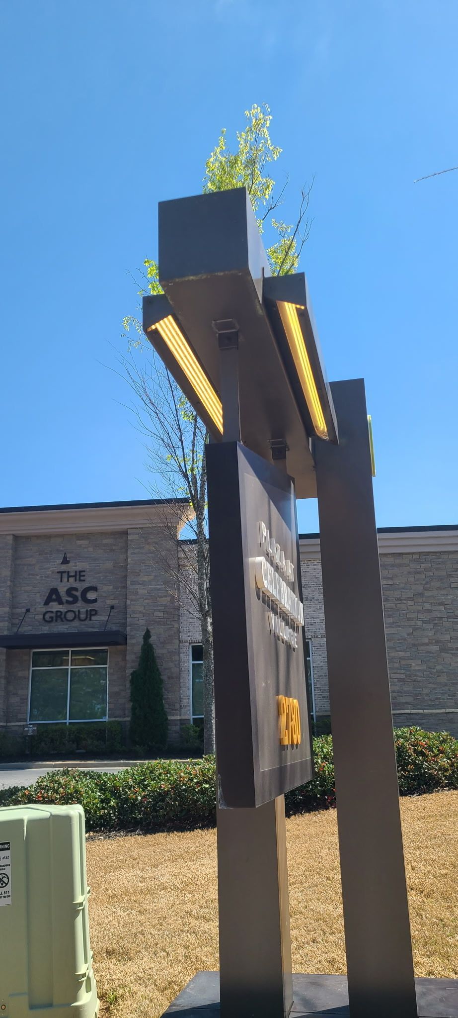 A modern sign with a light on top and a UPS logo on a brown sign. Blue sky and brick building.