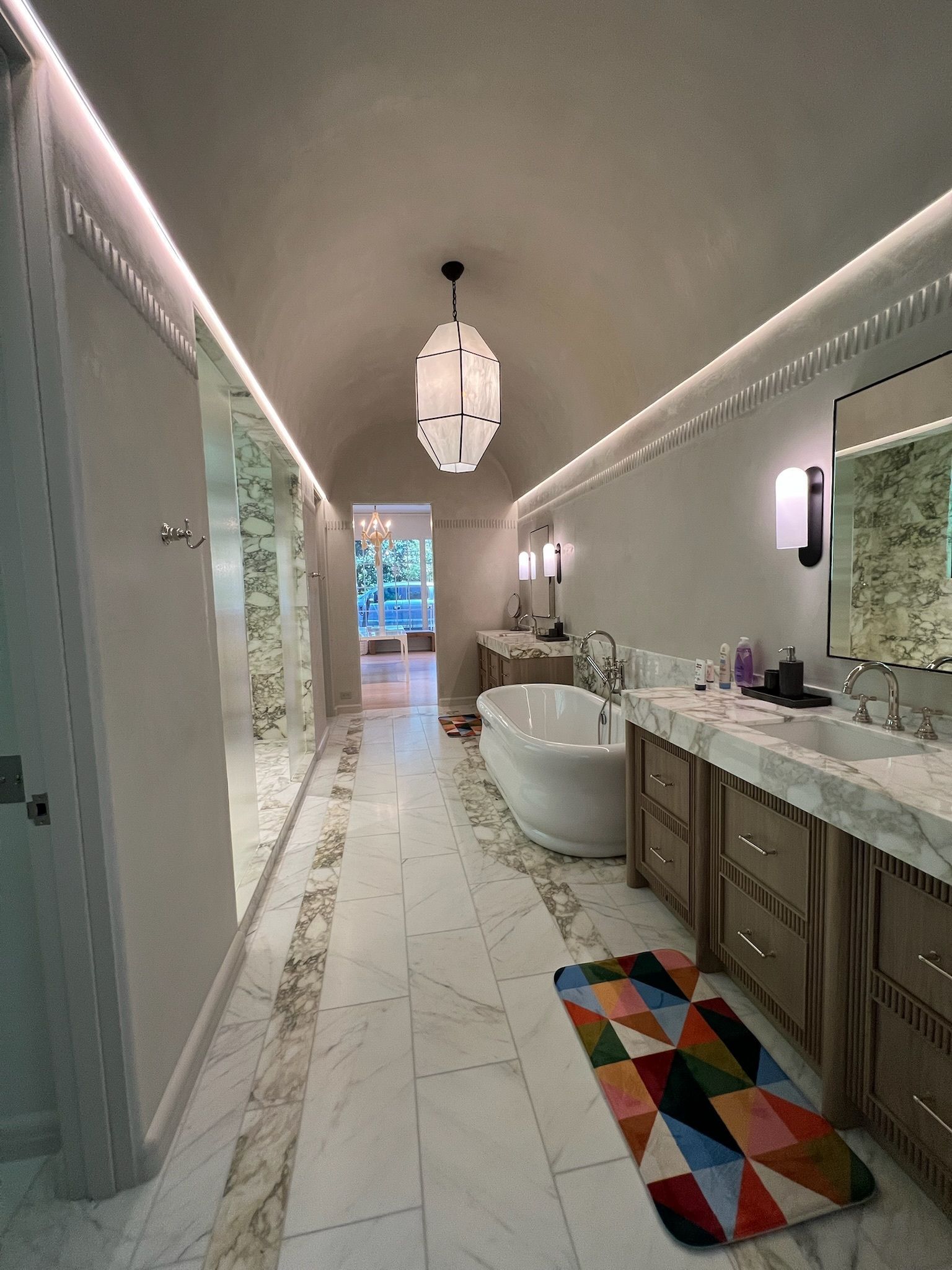 Spacious, luxurious bathroom with marble floors, a freestanding tub, and a colorful rug.