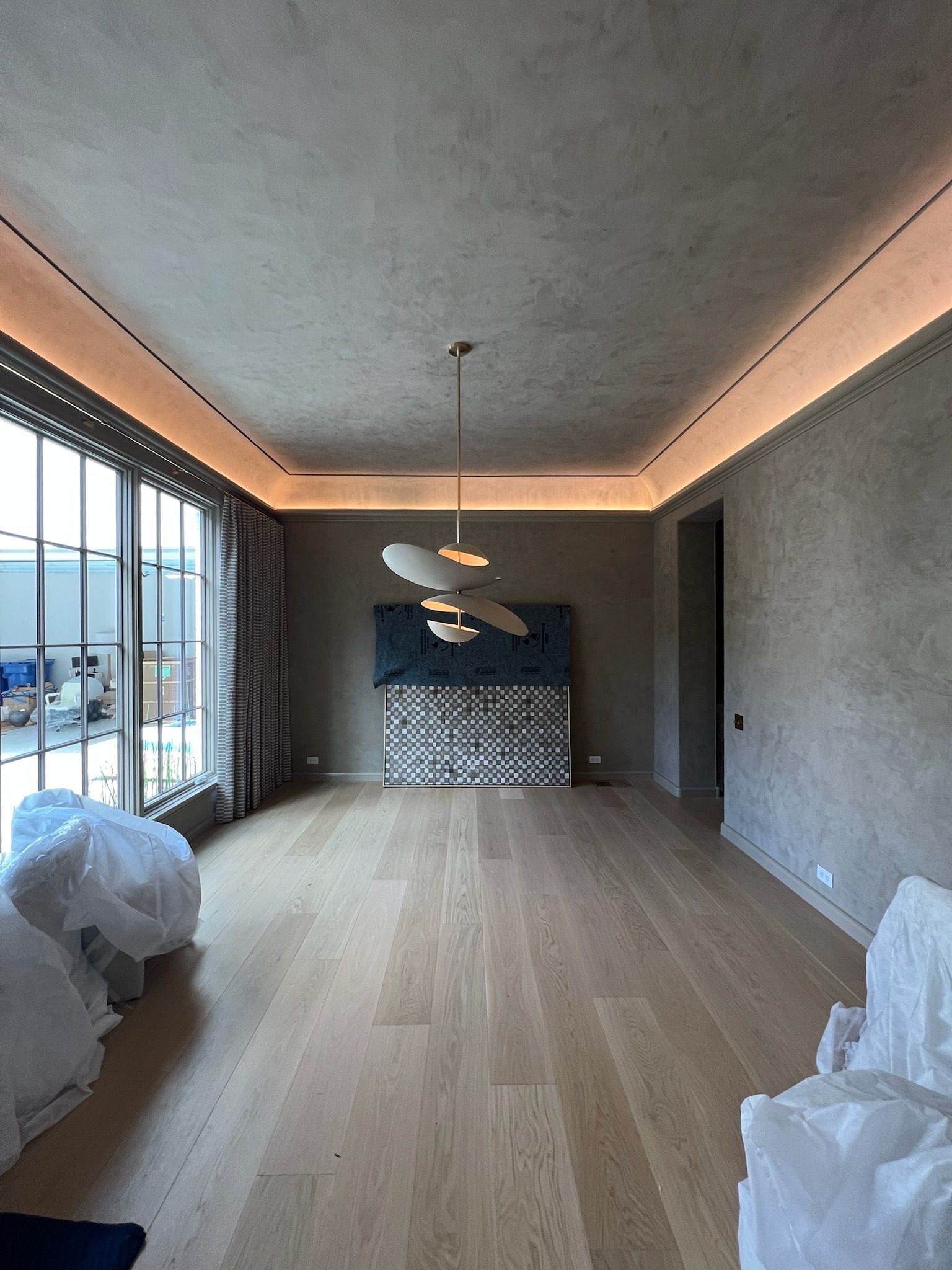 Empty room with wood floors, textured gray walls, large window, and modern light fixture.