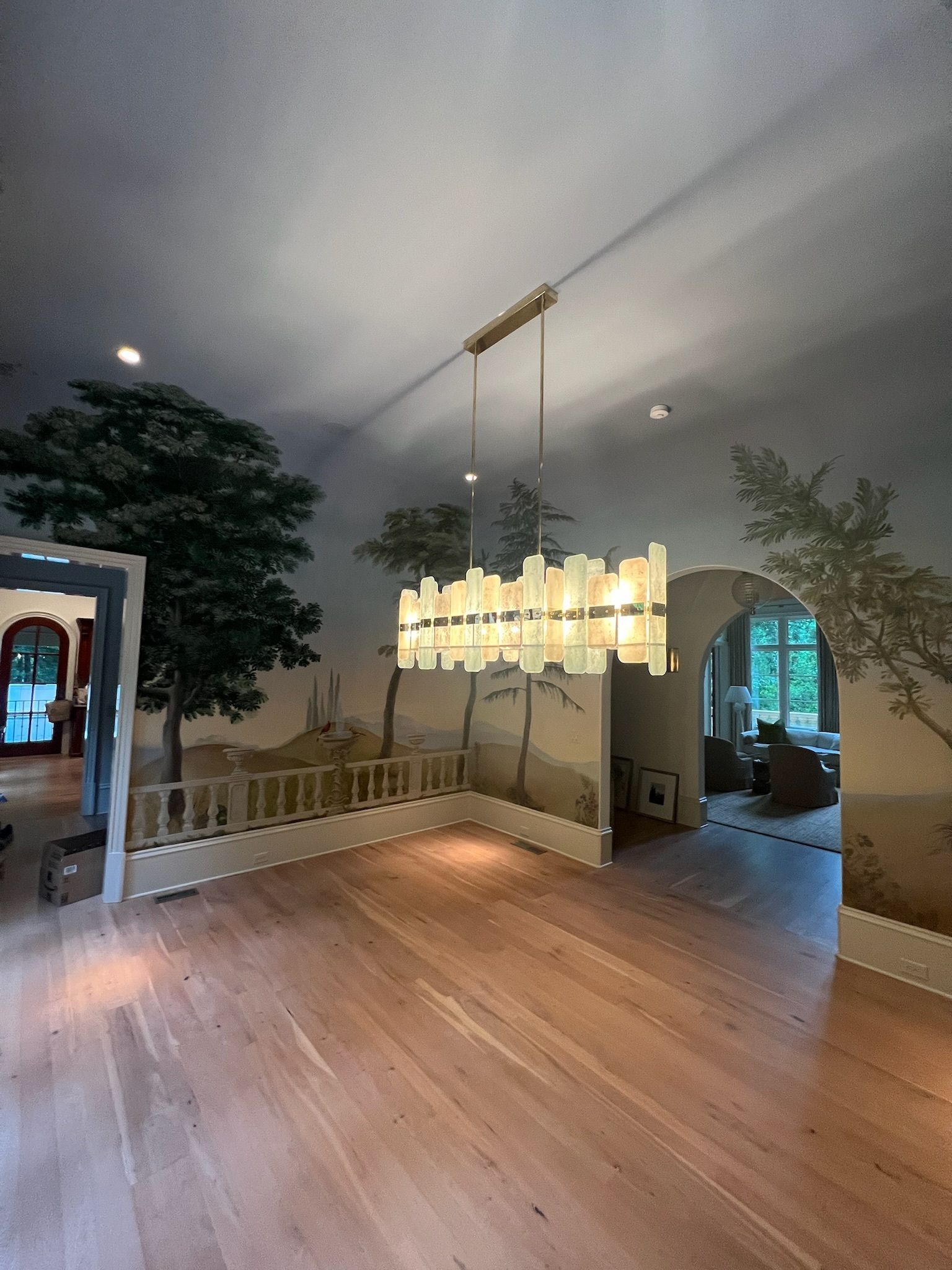 Interior of a room with wood floors, painted landscape mural, and large rectangular chandelier.