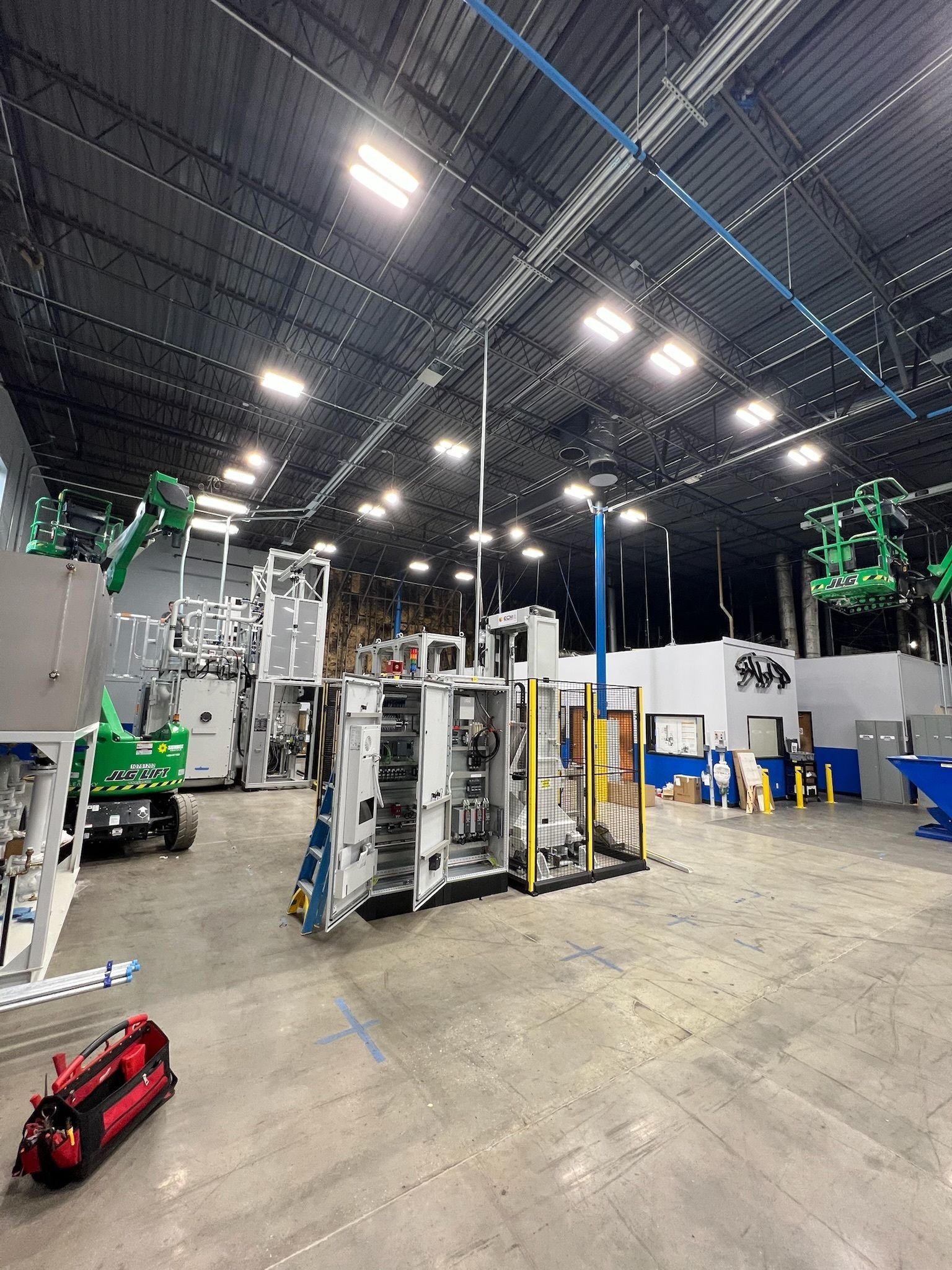 Large industrial warehouse with machinery, overhead lights, and a concrete floor.