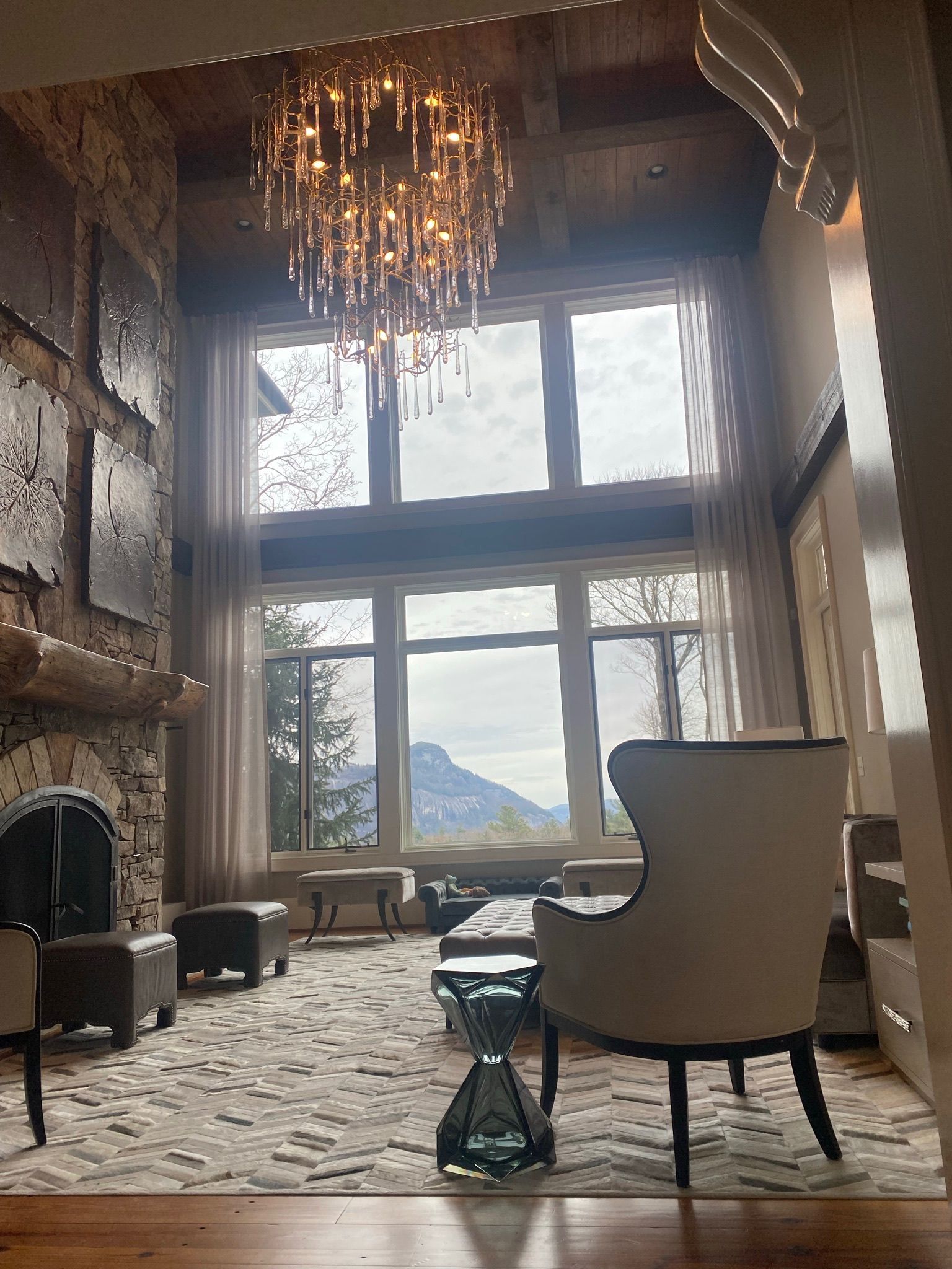 Living room with a large window, fireplace, and chandelier overlooking a mountain view.